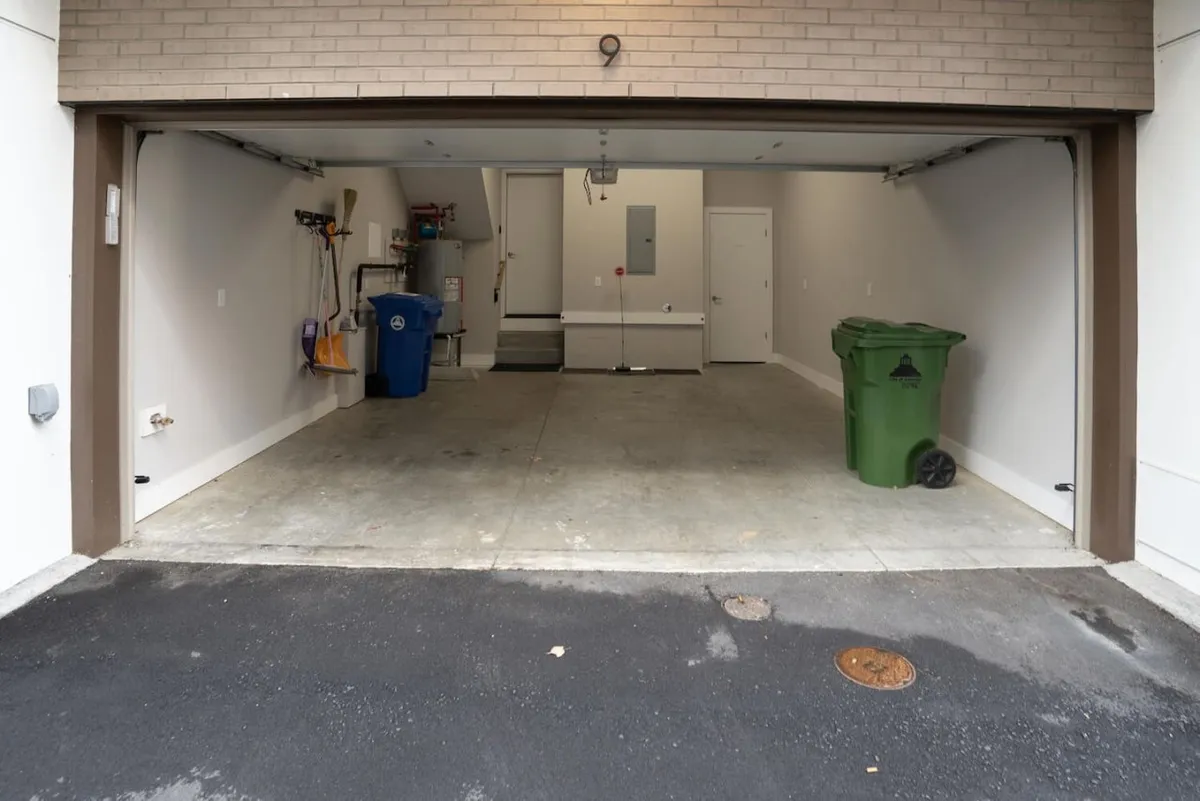 A view of the interior of the garage, featuring a clean concrete floor, a closed garage door, and organized bins for waste and recycling. The space is compact but functional, designed for convenience in urban settings.