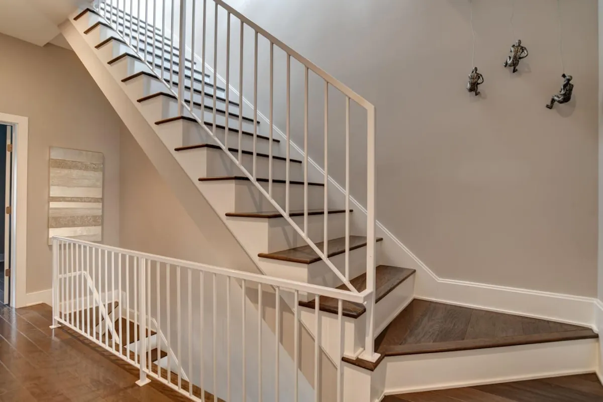A central staircase with a warm wooden railing and tasteful wall art forms the focal point of this image. It provides a view that is both welcoming and transitional, symbolizing movement through the multi-level home and the journey between shared and private spaces.