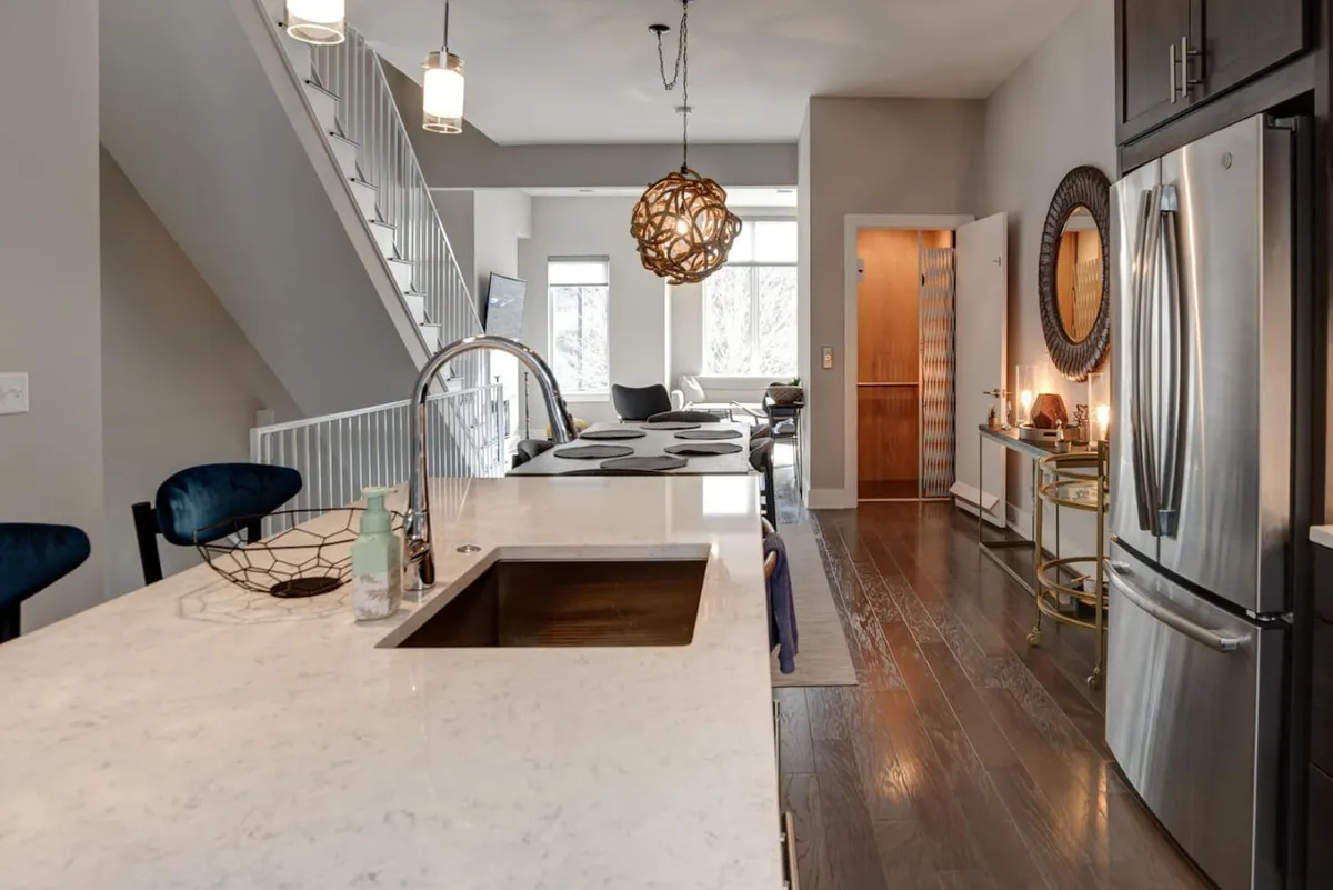 A spacious kitchen with a prominent island, sleek stainless steel appliances, pendant light fixtures, and an open layout. The kitchen is designed for both cooking and entertaining, with bar stools inviting conversation and casual dining, blending seamlessly with the adjoining living spaces.