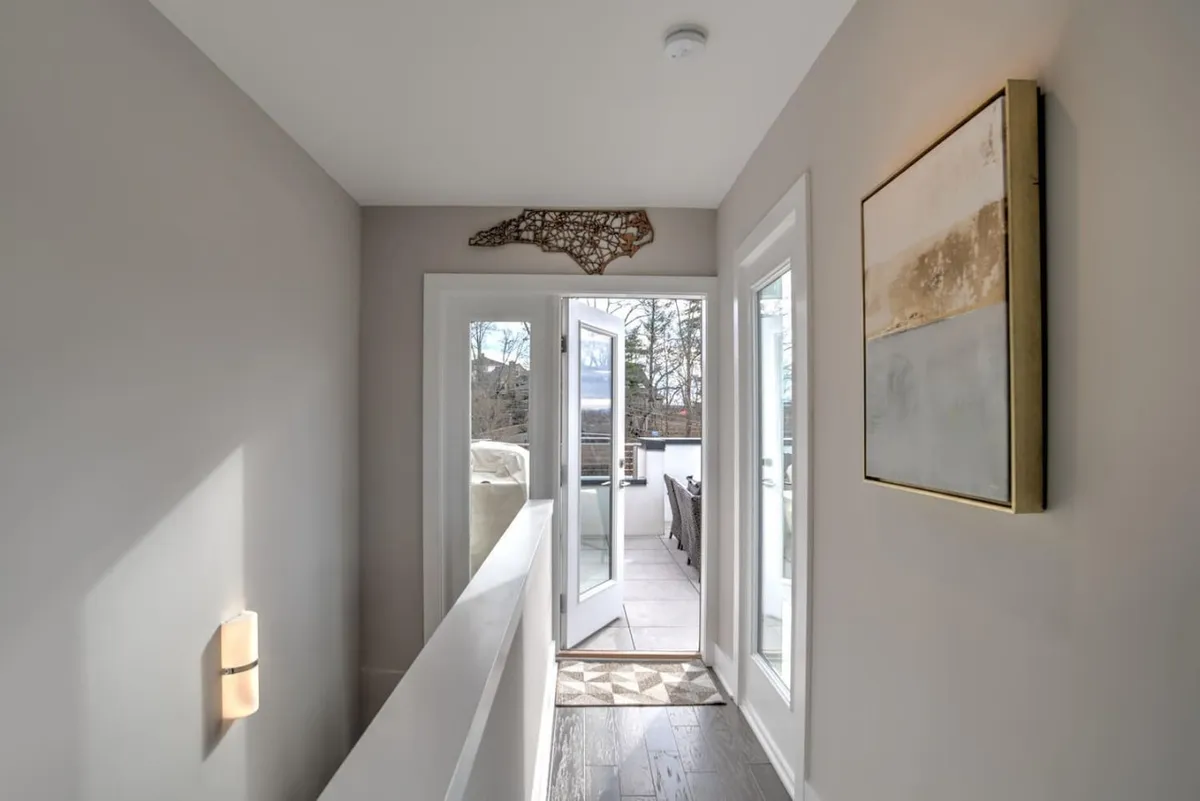 This image captures open doors revealing a sunlit space adorned with decorative wall art and framed artwork. The view hints at a seamless connection between interior comfort and the potential for gathering spaces, possibly leading to an outdoor terrace or offering a glimpse of the surrounding environment. The inviting atmosphere and natural light suggest relaxation and sociable moments.